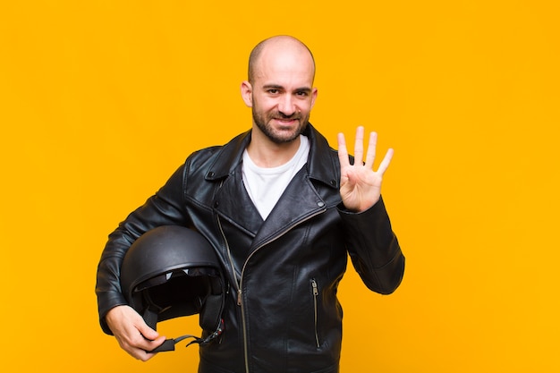 Jovem careca sorrindo e parecendo amigável, mostrando o número quatro ou o quarto com a mão para a frente, em contagem regressiva