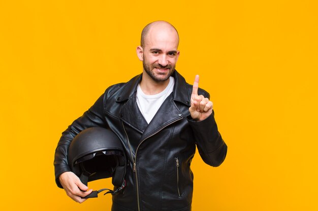 Jovem careca sorrindo e parecendo amigável, mostrando o número um ou o primeiro com a mão para a frente, em contagem regressiva