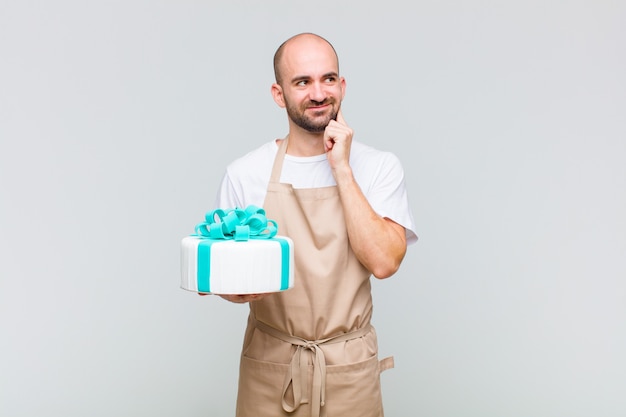 Jovem careca sorrindo feliz e sonhando acordado ou duvidando, olhando para o lado