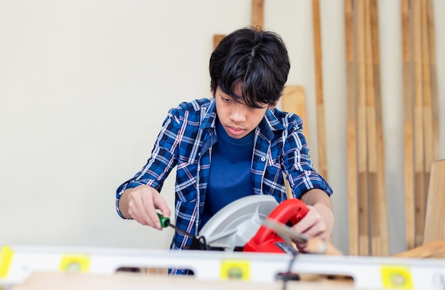 Jovem carpinteiro usando uma chave de fenda para consertar uma serra circular na oficina de carpintaria. criança aprendendo a trabalhar com madeira na oficina do artesão