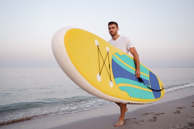 Jovem carregando prancha de supino após a sessão de surfe aquático