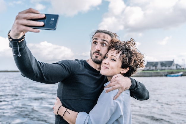 Jovem casal abraçou fazendo um selfie com o porto e o mar fora de foco