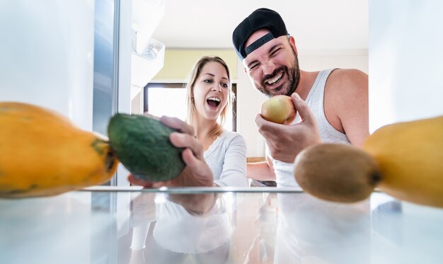 Jovem casal abre a geladeira em casa enquanto escolhe frutas orgânicas para smoothie fresco