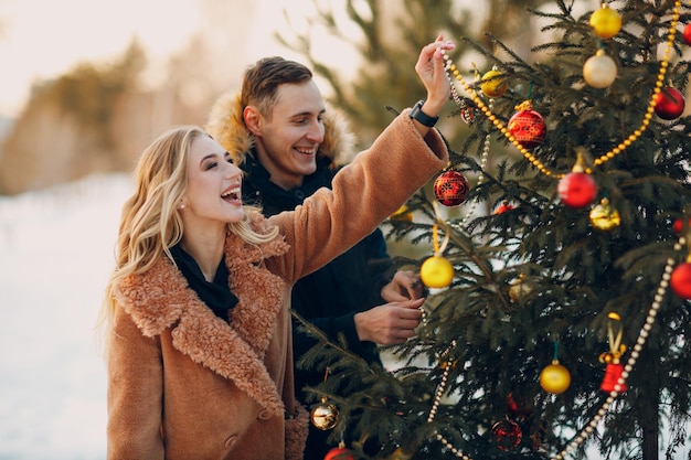 Jovem casal adulto decora a árvore de natal na floresta de inverno Conceito de celebração de festa de pinho de ano novo