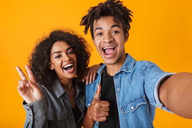 Jovem casal africano alegre parado isolado, tirando uma selfie