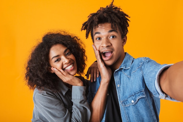 Jovem casal africano alegre parado isolado, tirando uma selfie