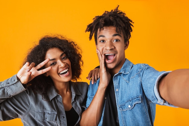 Jovem casal africano alegre parado isolado, tirando uma selfie