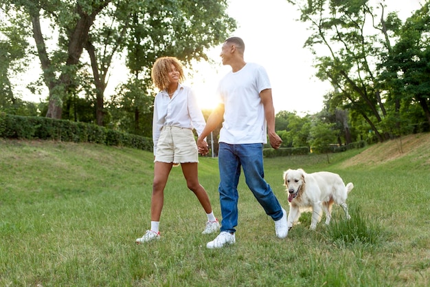 Jovem casal afro-americano fica junto com cachorro e de mãos dadas no parque