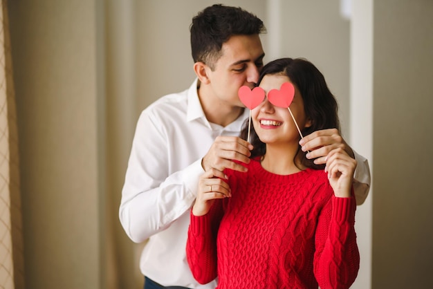 Jovem casal alegre apaixonado segurando corações vermelhos sobre os olhos e sorrindo