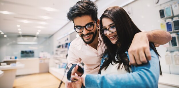 Jovem casal alegre lindo está navegando relógios de mão em uma loja de tecnologia