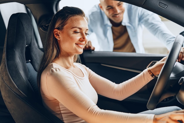 Jovem casal alegre olhando ao redor dentro de um carro novo que vai comprar em uma loja de automóveis