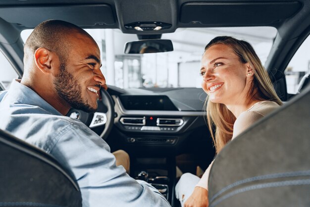 Jovem casal alegre olhando ao redor dentro de um carro novo que vai comprar em uma oficina