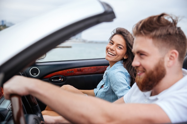 Jovem casal alegre sorrindo enquanto dirigia seu carro conversível