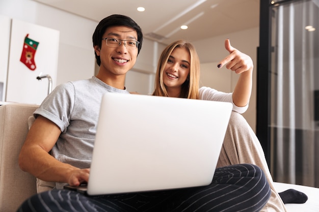 Jovem casal alegre, usando laptop enquanto está sentado em um sofá em casa