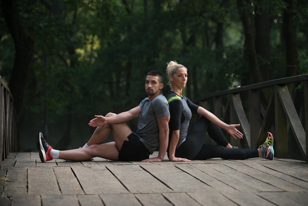 Jovem casal alongamento antes de correr na área de floresta arborizada - treinamento e exercício para Trail Run Maratona Endurance - conceito de estilo de vida saudável de fitness