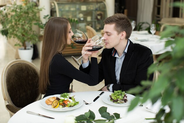 Jovem casal amoroso feliz comemorando com vinho tinto no restaurante.