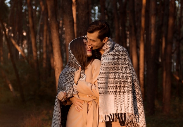 Jovem casal apaixonado, abraçando e beijando coberto de manta na floresta de outono. Homem feliz e mulher tendo encontro romântico