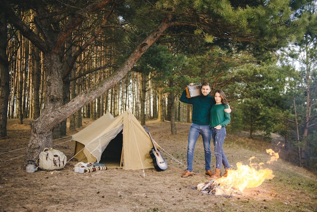 Jovem casal apaixonado acampar turistas sentado perto de um incêndio contra uma tenda na floresta ouvindo rádio retrô