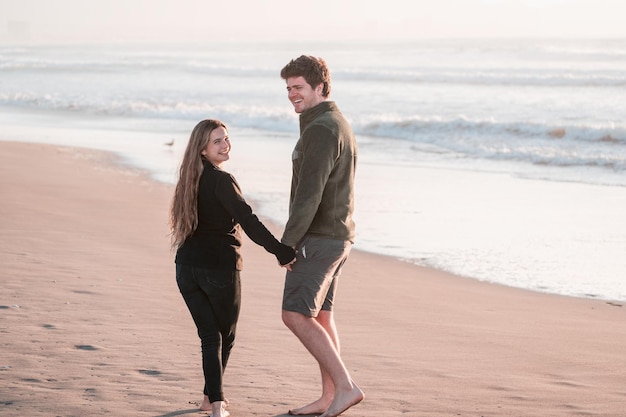 Jovem casal apaixonado caminhando na praia de mãos dadas sorrindo feliz