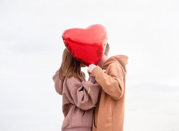 Foto jovem casal apaixonado com balões vermelhos se abraçando e se beijando ao ar livre