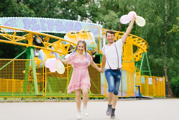 Foto jovem casal apaixonado corre com balões e se diverte em um parque de diversões