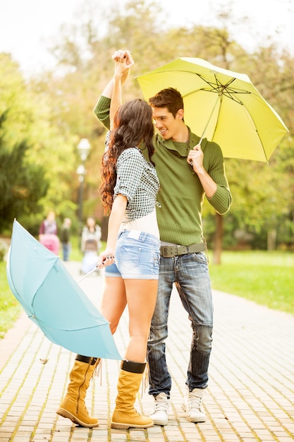 Foto jovem casal apaixonado, dançando no parque com guarda-chuvas nas mãos.