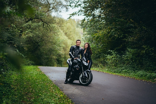 Jovem casal apaixonado em roupas de couro preto perto de uma motocicleta esportiva preta na estrada