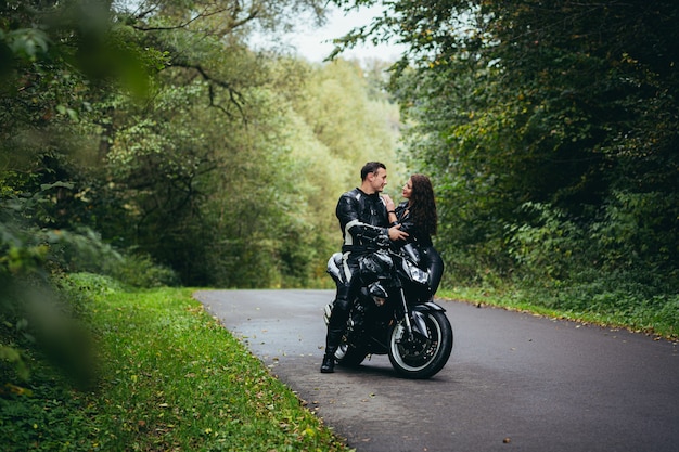 Jovem casal apaixonado em roupas de couro preto perto de uma motocicleta esportiva preta na estrada