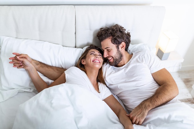 Foto jovem casal apaixonado na cama. jovem casal deitado na cama e rindo enquanto faz cócegas um no outro. casal jovem e feliz e sensual, deitado na cama pela manhã