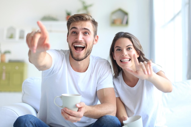 Jovem casal apaixonado no sofá em casa assistindo tv e rindo.