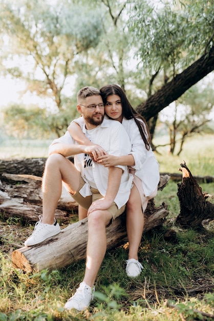 Jovem casal apaixonado por um cara com barba e uma garota com cabelo escuro em roupas leves na floresta verde