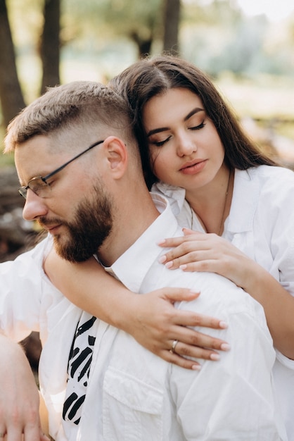 Jovem casal apaixonado por um cara com barba e uma garota com cabelo escuro em roupas leves na floresta verde