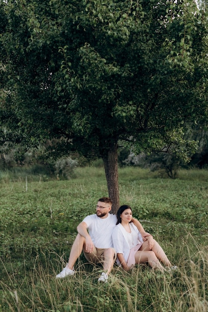 Jovem casal apaixonado por um cara com barba e uma garota com cabelo escuro em roupas leves na floresta verde