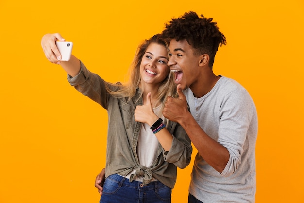 Jovem casal apaixonado posando isolado na parede amarela, tirando uma selfie