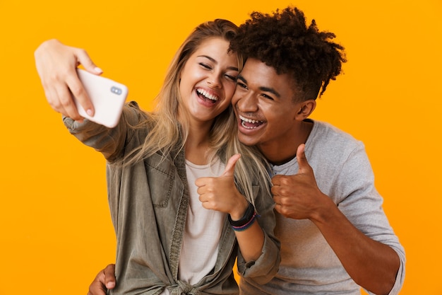 Jovem casal apaixonado posando isolado na parede amarela, tirando uma selfie