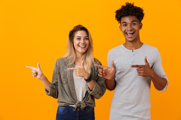 Jovem casal apaixonado posando isolado sobre uma parede amarela apontando