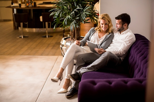 Foto jovem casal apaixonado sentado no sofá e lookind na tabuleta digital