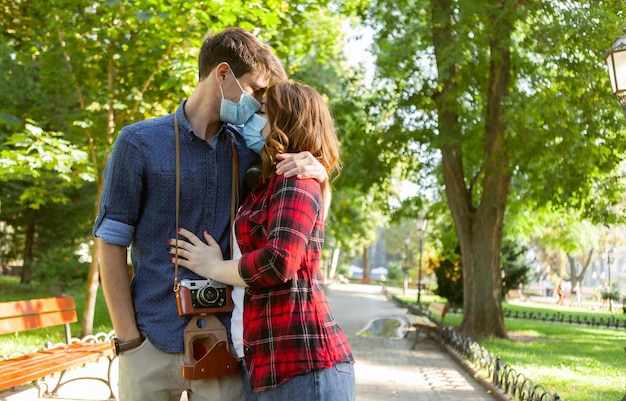 Jovem casal apaixonado, turista de homem e mulher se beijando com máscara médica protetora no rosto externo. coronavírus pandêmico (covid-19), conceito de viagem