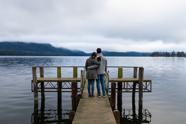 Jovem casal asiático abraçando encostado no ombro na ponte Lago Te Anau Nova Zelândia
