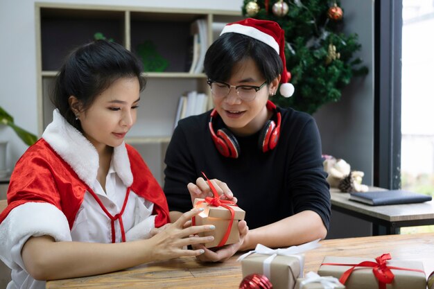 Jovem casal asiático abrindo a caixa de presente de Natal juntos na sala de estar.