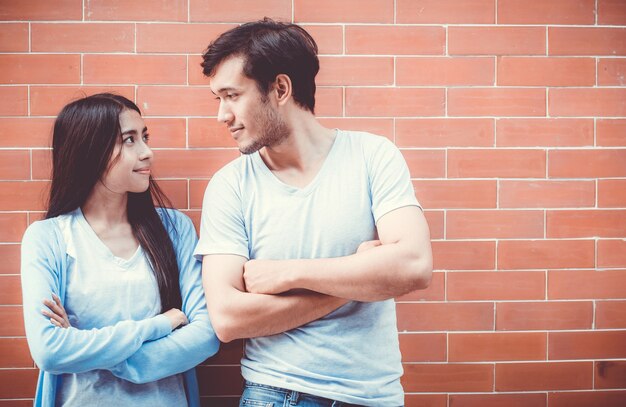 Jovem casal asiático atraente olhando rosto e sorrindo contra a parede de tijolos