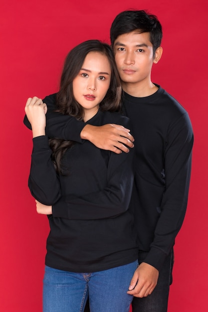 Jovem casal asiático atraente vestindo jeans e camisa preta contra um fundo vermelho.