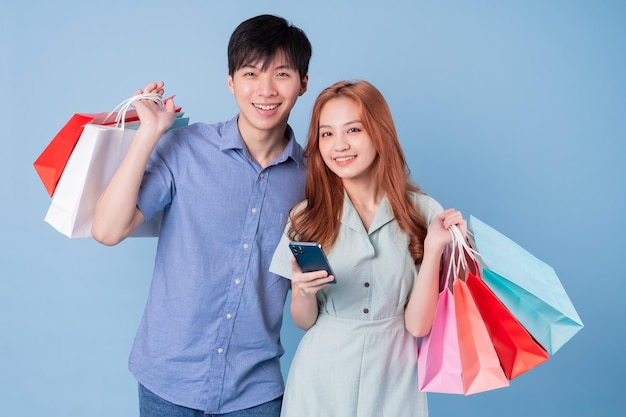 Jovem casal asiático carregando sacola de compras em fundo azul