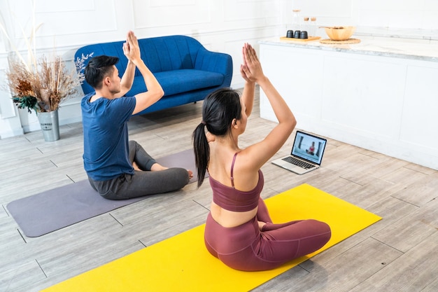 Jovem casal asiático e esportivo assistindo aula de ioga ao vivo ou vídeo tutorial em casa