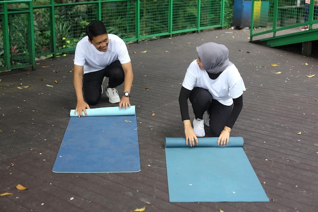 Jovem casal asiático falando enquanto rolando esteira de pilates de ioga após treino no parque. Estilo de vida saudável