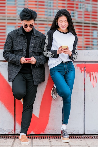 Jovem casal asiático feliz usando smartphone em uma rua da cidade