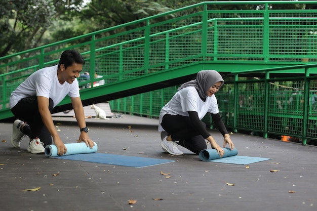 Jovem casal asiático rolando esteira de pilates de ioga após workput no parque. Casal de estilo de vida saudável conc