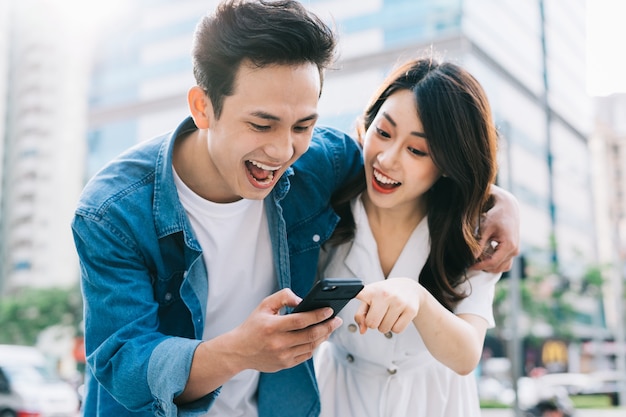 Jovem casal asiático usando smartphone juntos na rua