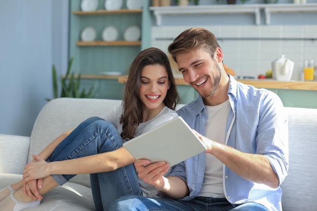 Jovem casal assistindo conteúdo de mídia online em um tablet sentado em um sofá na sala de estar.