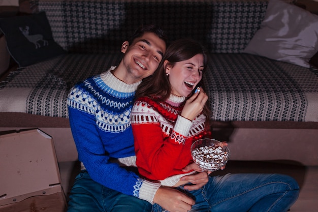 Jovem casal assistindo filme comendo pipoca em casa à noite